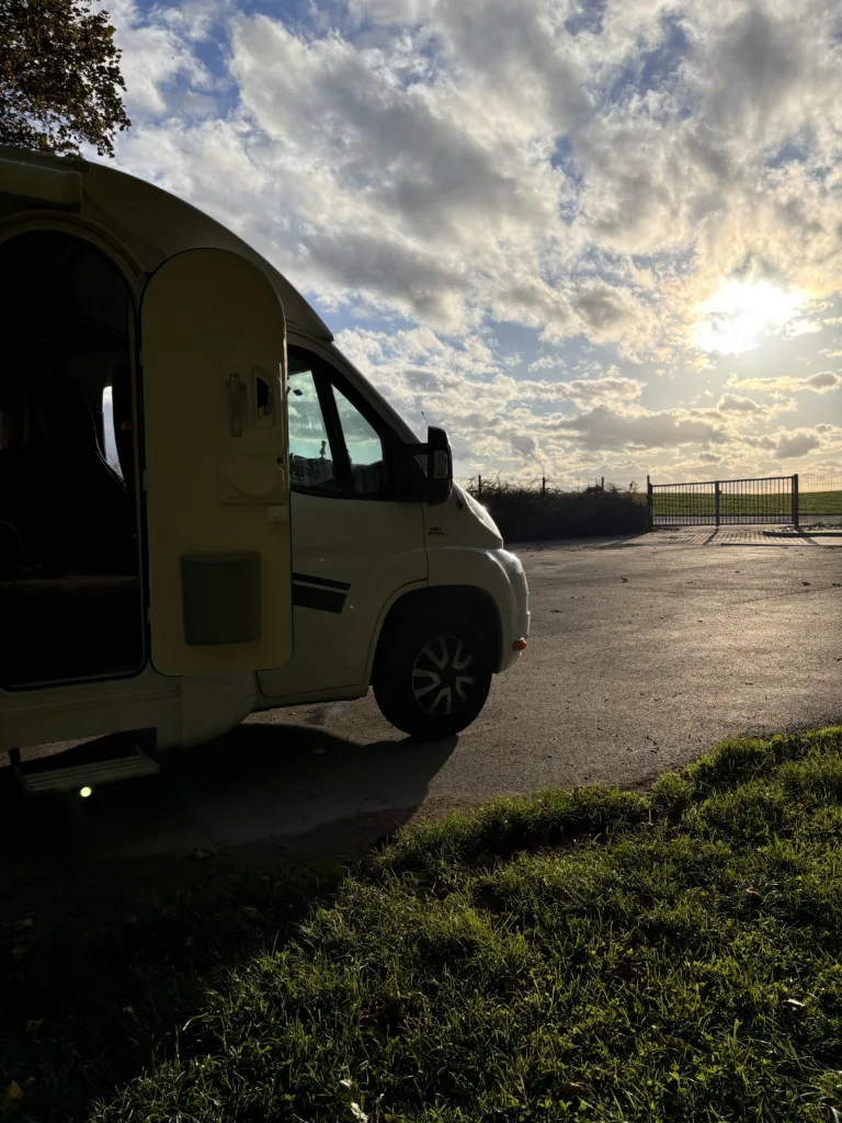Witte camper met deur open met op de achtergrond een wolkenlucht en een ondergaande zon